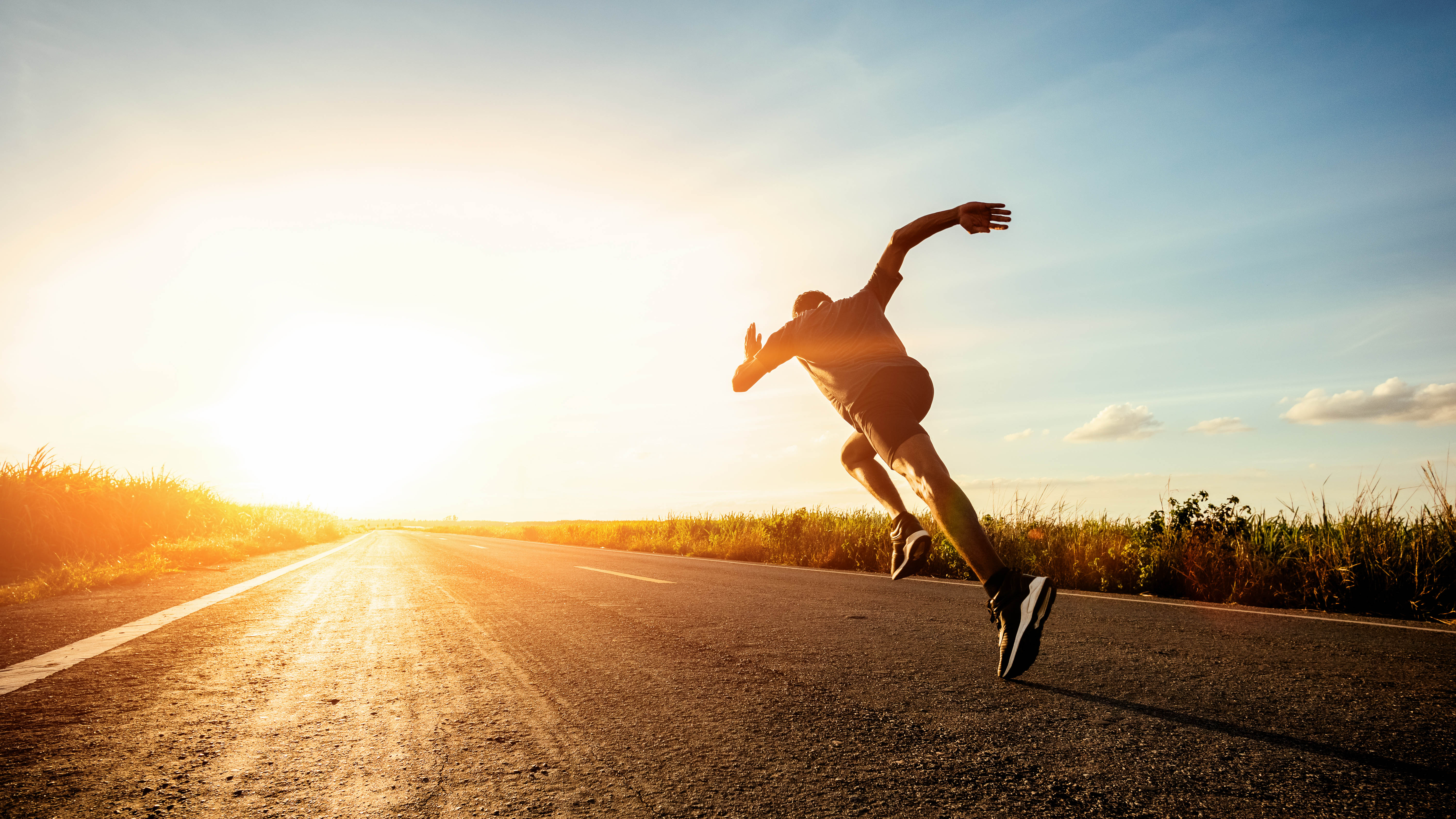 Fit man running along a back-country road, seemingly running right into the sunset.